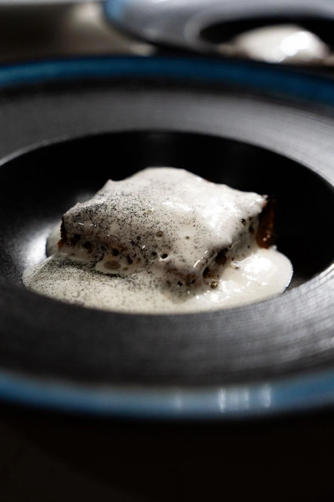 Plated dish with foam and charcoal dust in a dark ceramic bowl