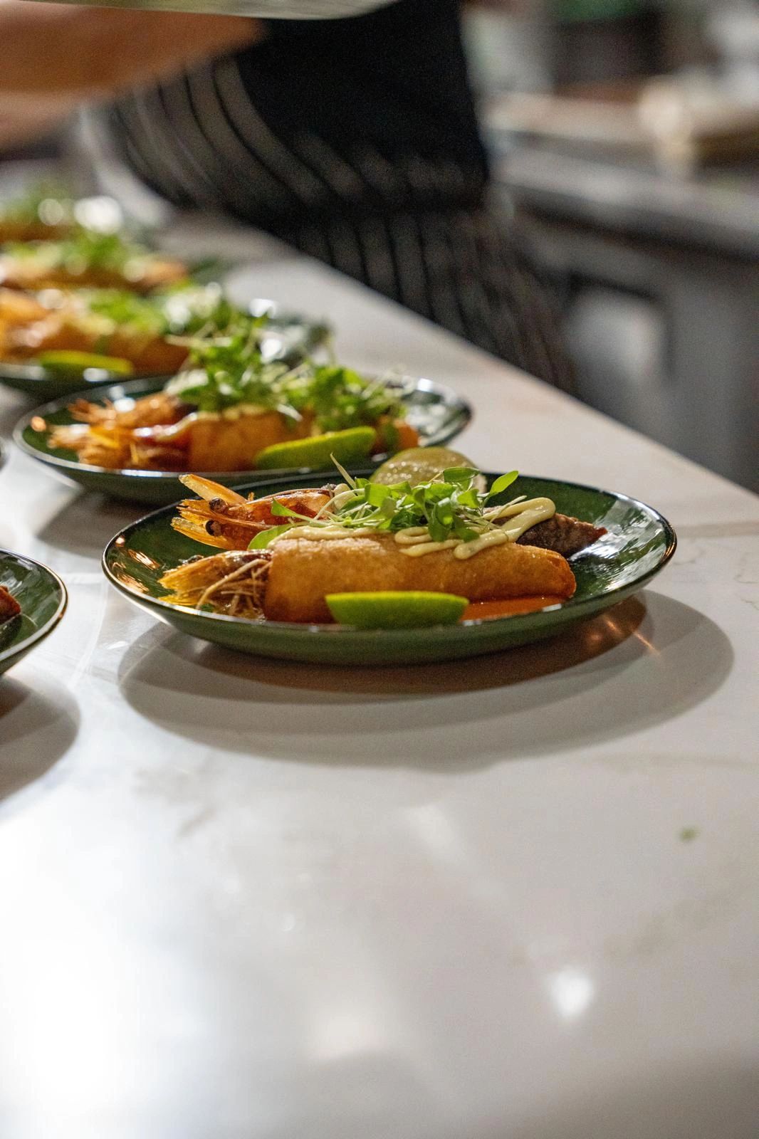 Line of finished plates with fried shrimp, lime and microgreens on the kitchen pass