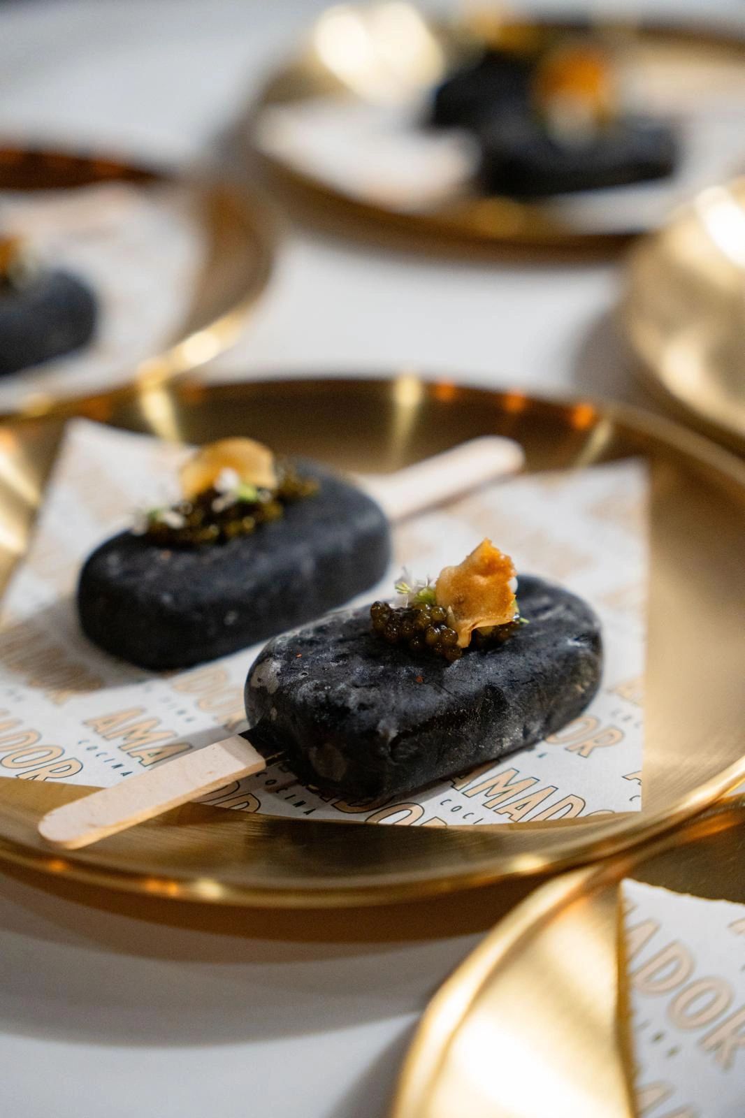 Black caviar-topped paletas served on gold plates over Amador-branded paper
